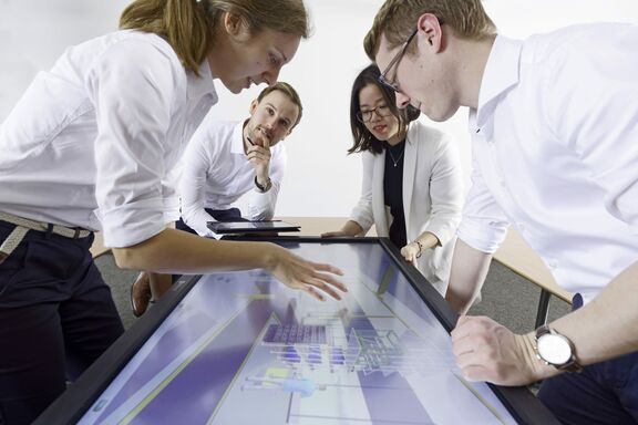 Auf dem Foto sind insgesamt vier Personen, zwei Frauen und zwei Männer. Sie beugen sich über einen Monitor mit einem technischen Modell.