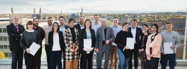 17 Menschen, darunter Rektor Rüdiger und die vertreter*innen der geförderten Projekte, lächeln in die Kamera. Im Hintergrund befinden sich die Aachener Innenstadt mit Dom und Rathaus.