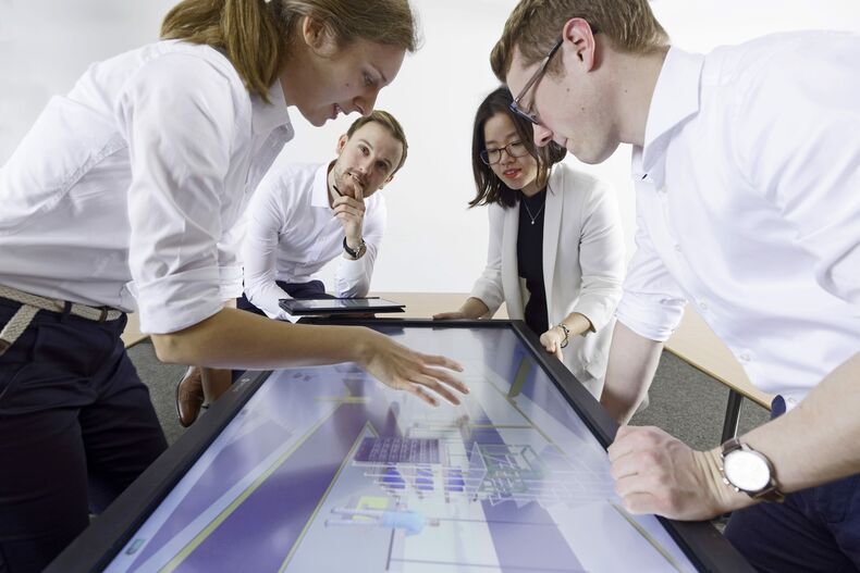 Auf dem Foto sind insgesamt vier Personen, zwei Frauen und zwei Männer. Sie beugen sich über einen Monitor mit einem technischen Modell.