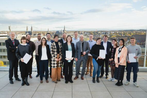 17 Menschen, darunter Rektor Rüdiger und die vertreter*innen der geförderten Projekte, lächeln in die Kamera. Im Hintergrund befinden sich die Aachener Innenstadt mit Dom und Rathaus.
